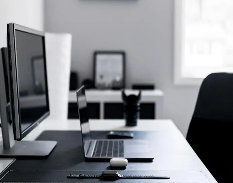 A desk with a laptop and two monitors in a bright office